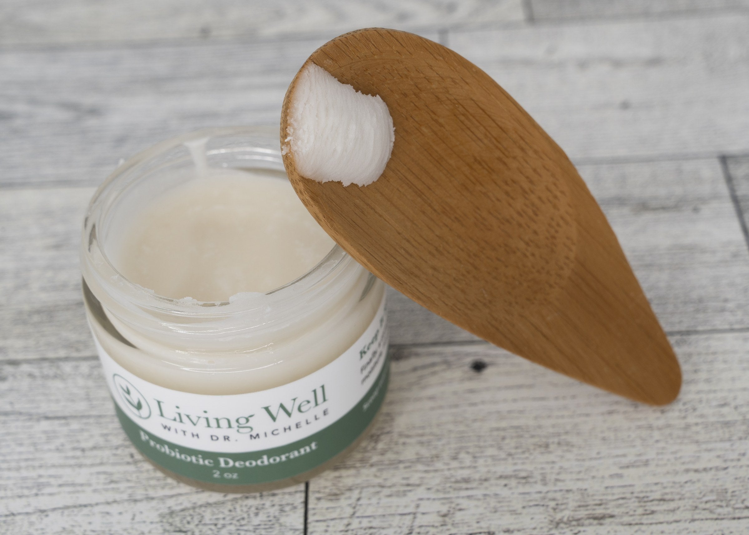 Living Well Probiotic Deodorant cream in an open jar with a wooden applicator scooping the natural formula