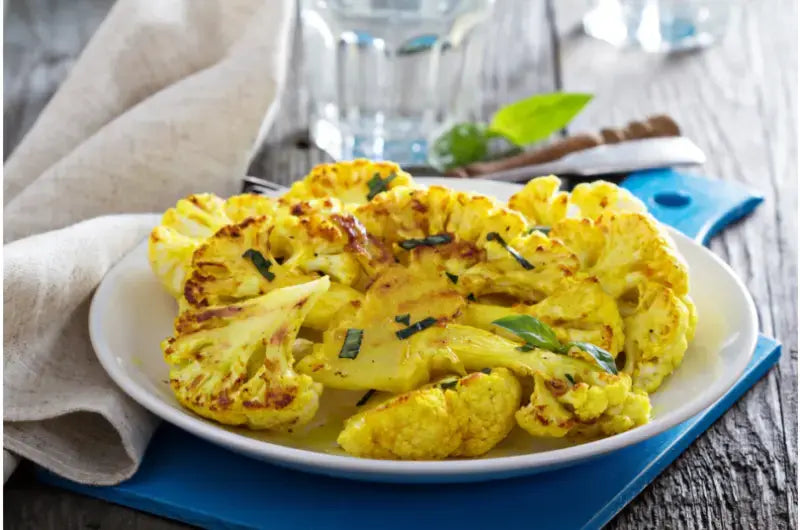 Whole roasted melt in your mouth cauliflower, golden and crisped at the edges, on a serving plate