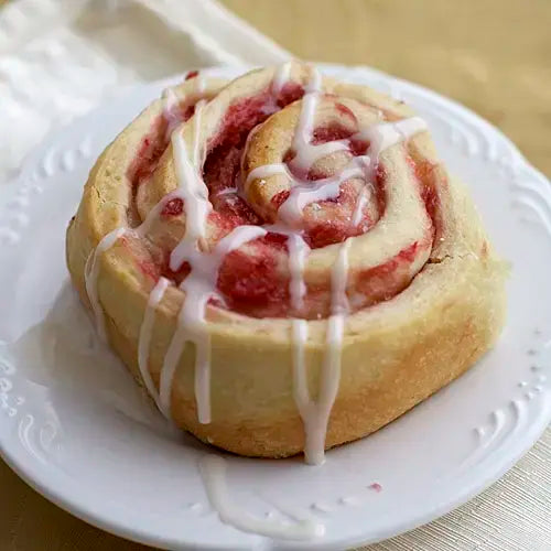 A rhubarb sweet roll on a white plate, drizzled with lemon rhubarb glaze
