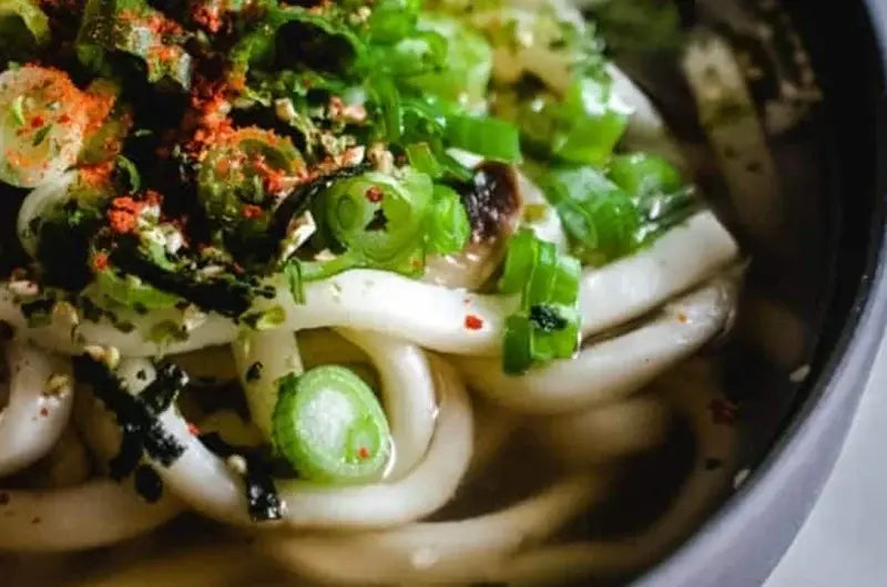 Bowl of spring roll soup with udon noodles, cabbage, carrots, peppers, and green onions in a savory sesame broth