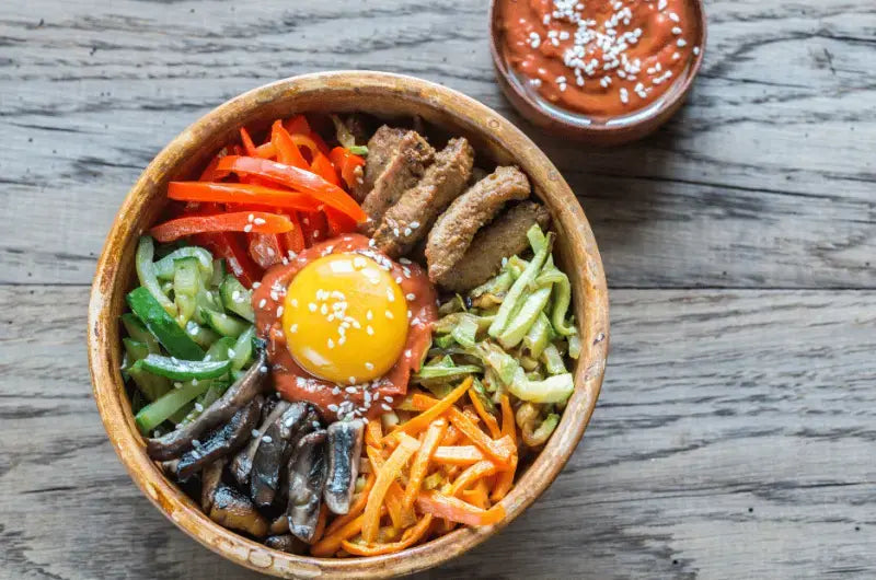 A bowl of homemade Korean bibimbap with rice, slow cooker beef, seasoned vegetables, and a fried egg on top